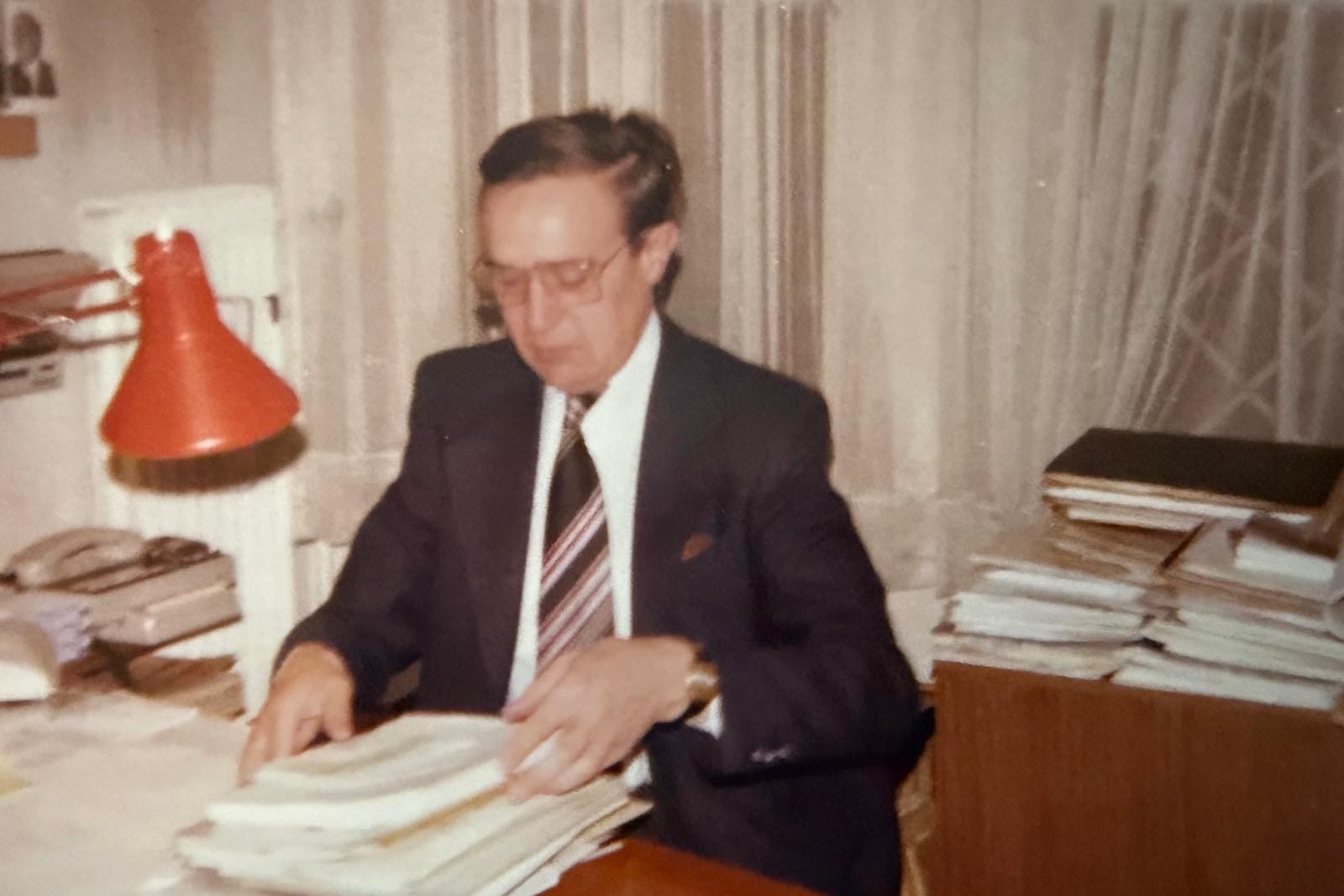 Karl-Josef Luthe im Anzug am Schreibtisch, vor ihm Papierstapel, daneben eine orange Schreibtischlampe